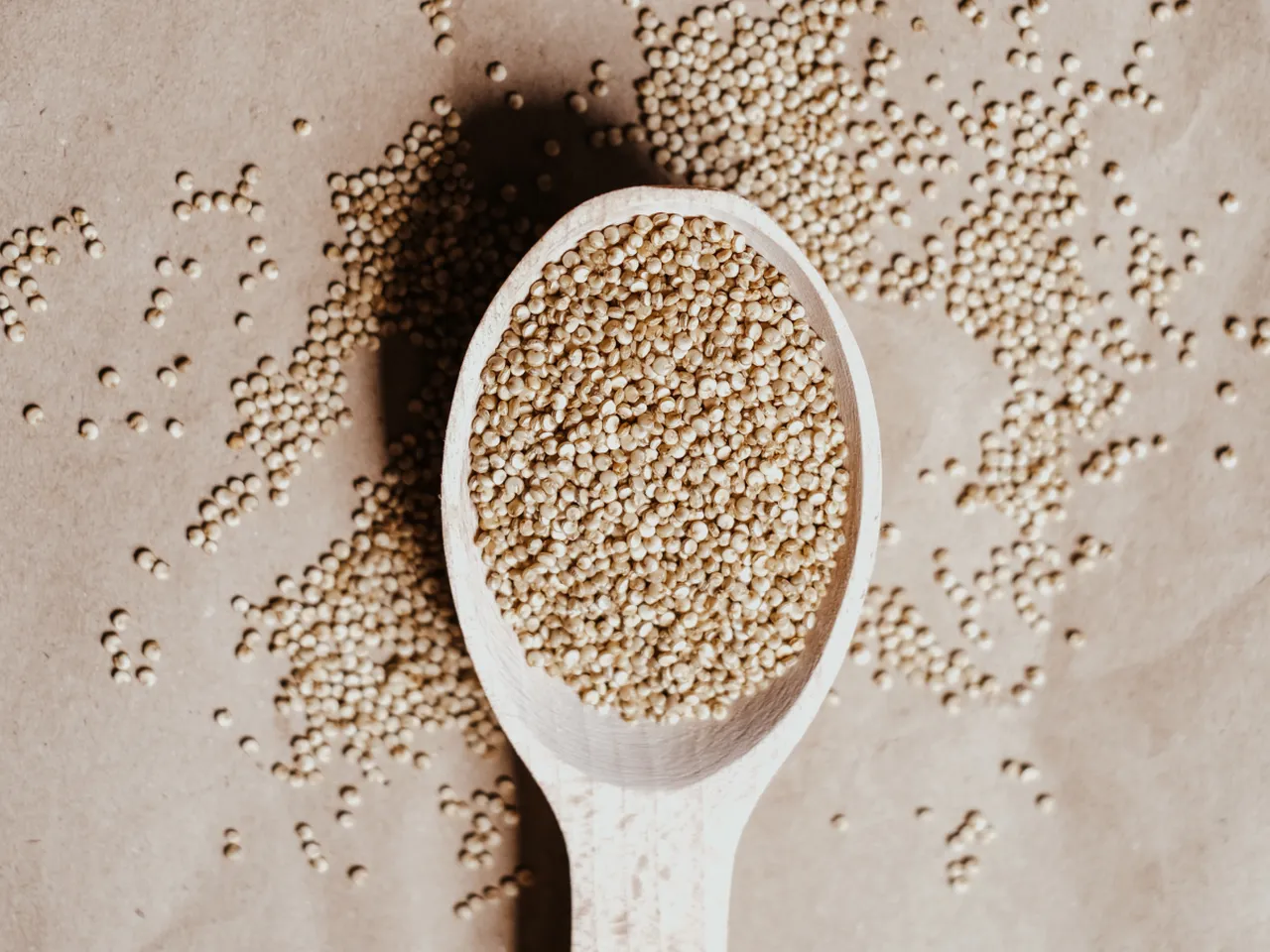 Wooden spoon filled with quinoa seeds on a parchment background, with scattered seeds around.