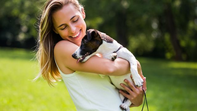 woman in park holding black and white puppy