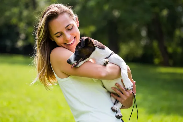 woman in park holding black and white puppy