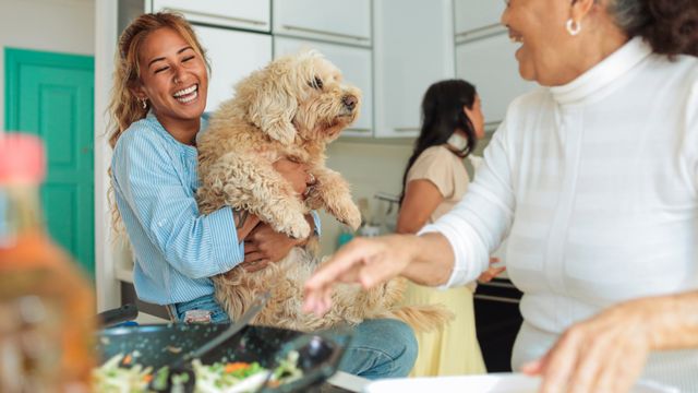 two ladies laughing while serving up food in the kitchen, one is holding a cavoodle